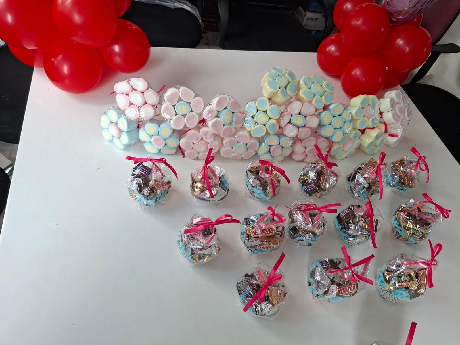 Mesa con dulces envueltos, bombones y clusters de globos rojos y blancos para baby shower