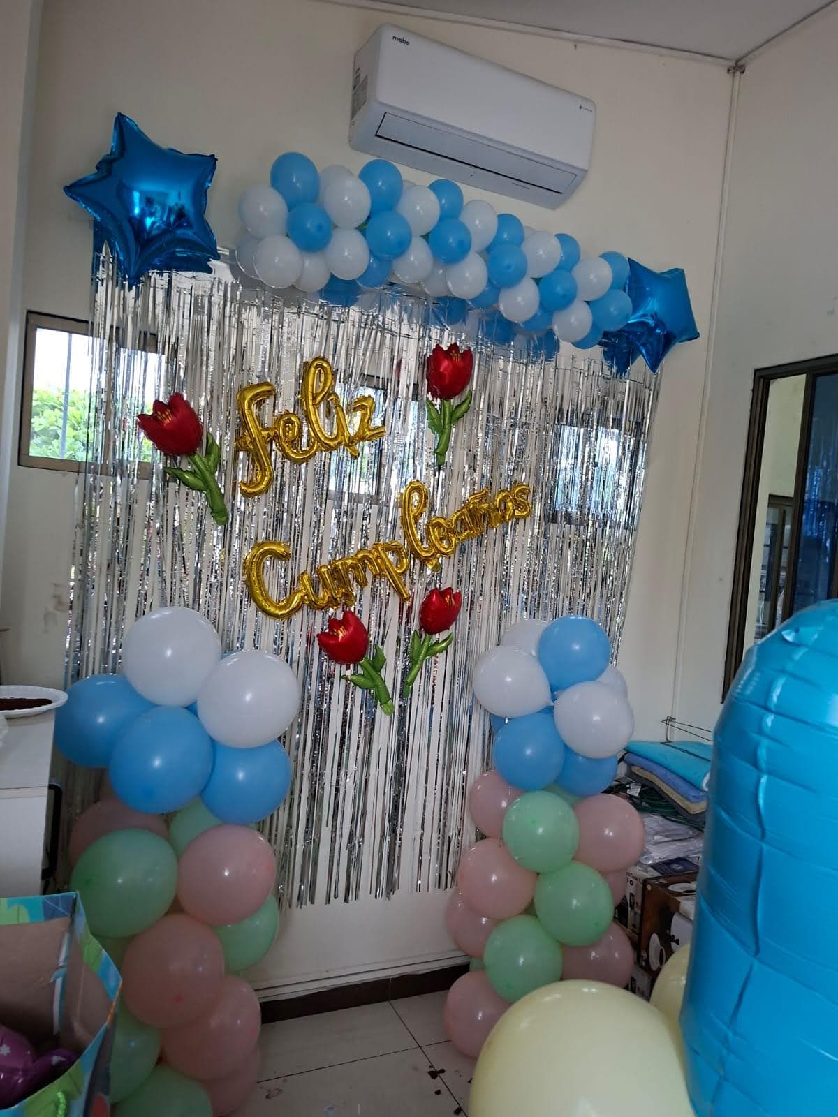 Pared decorada con letras doradas de Feliz Cumpleaños y guirnaldas de globos celestes