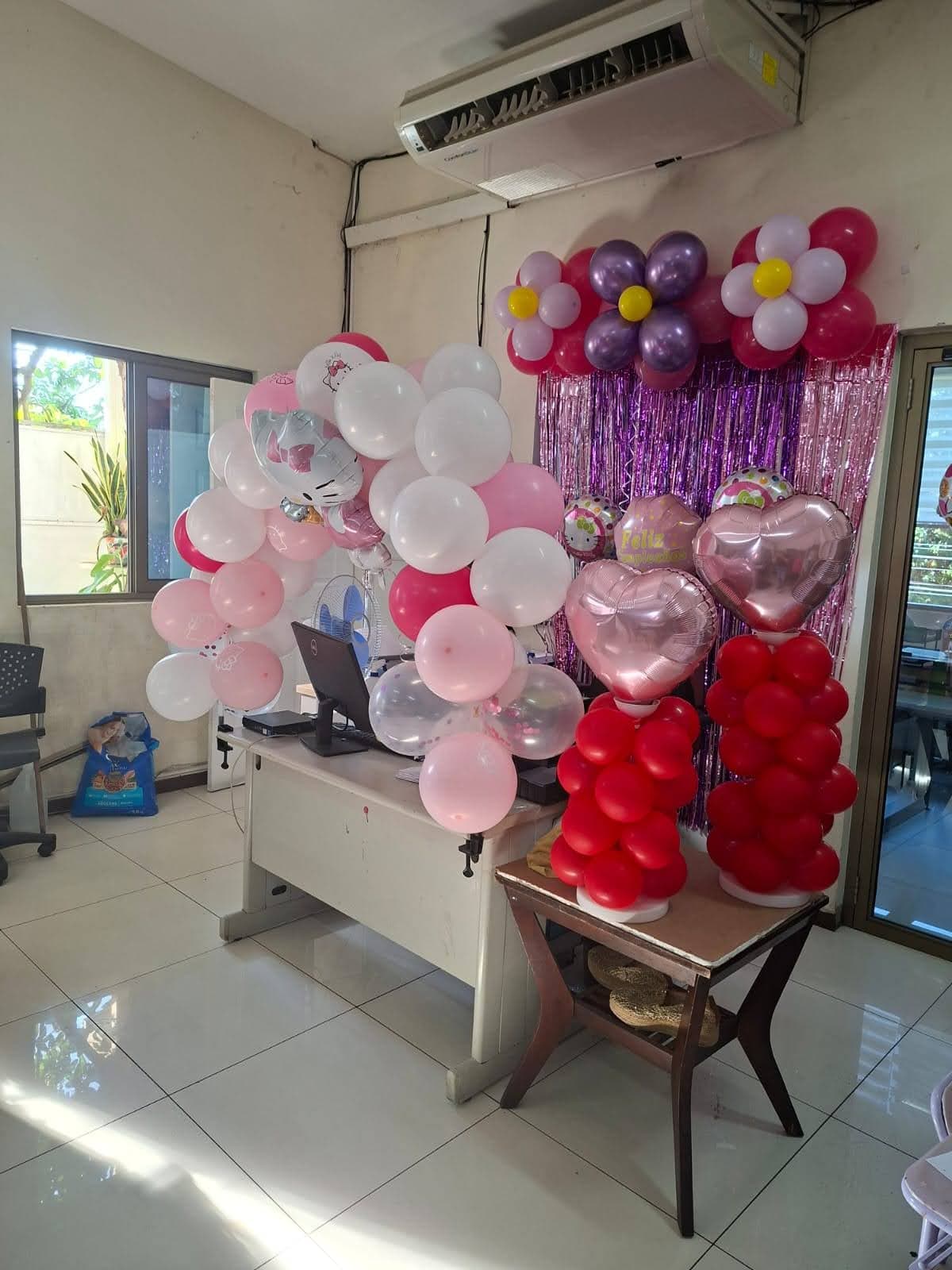 Decoración de oficina con arco de globos en rosas, morados y flores para festejo corporativo
